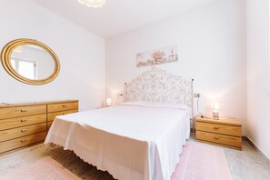 A bedroom with a bed, a wooden dresser, a nightstand, a mirror, and a wall-mounted picture.