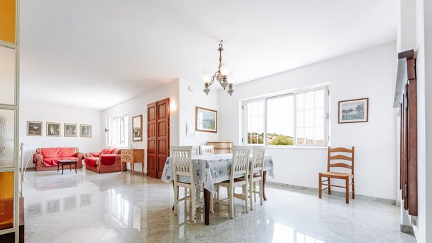 A spacious room with a dining table, chairs, a chandelier, and a large window. - Villa 'Casa Antonietta' with Private Terrace and Shared Garden (Sant'Anna Arresi)