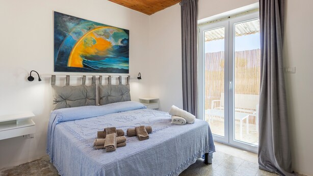 Ein Schlafzimmer mit einem Bett, einem Gemälde, einem Fenster und Blick ins Freie.