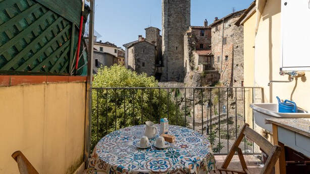 Un balcón con una mesa dispuesta para dos, vista a edificios históricos de piedra y un castillo al fondo.