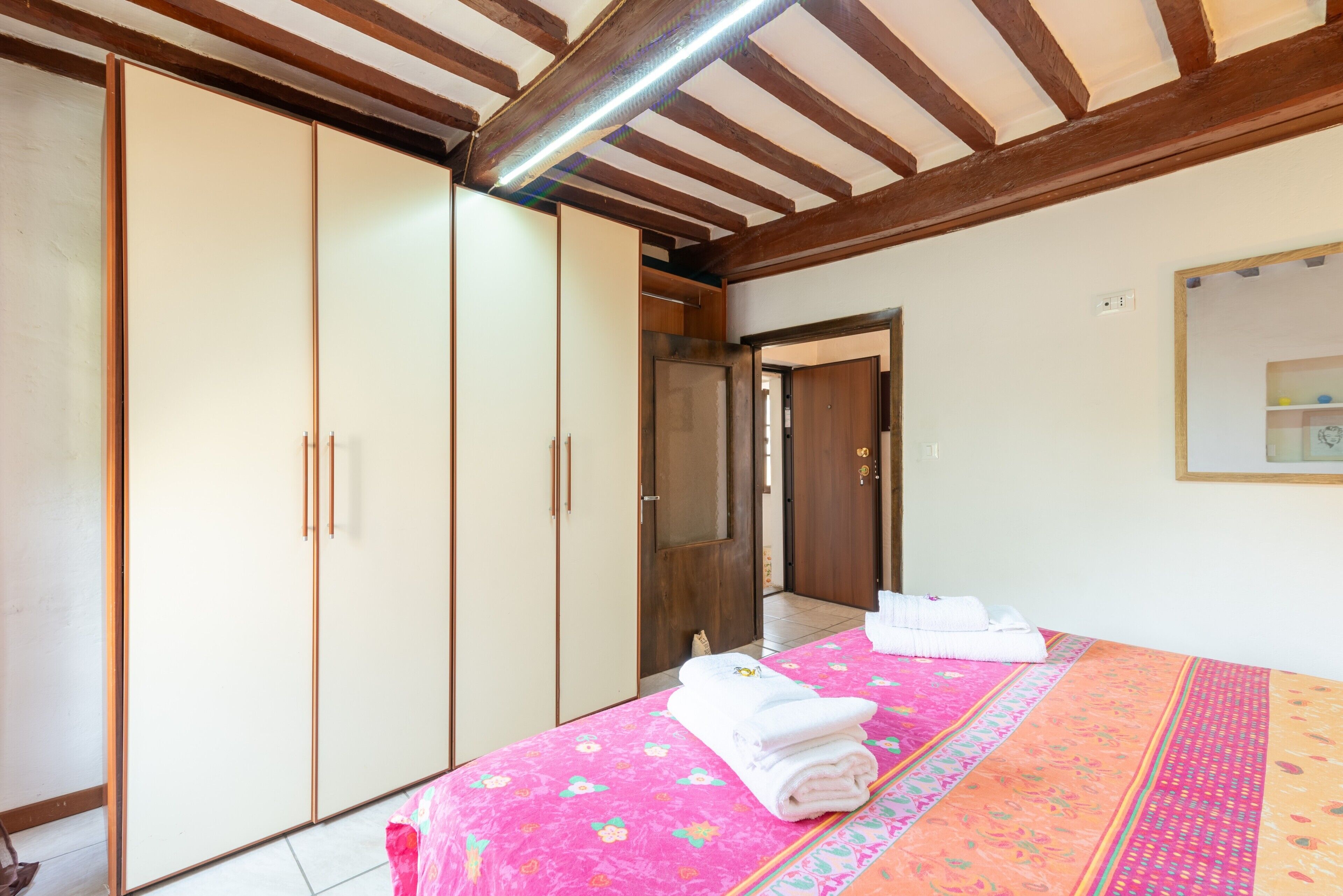 A bedroom with a bed, a wardrobe, a mirror, and a door leading to another room.