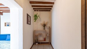 Un pasillo estrecho con suelo de madera, pared blanca, un estante de madera con plantas y un cuadro enmarcado.