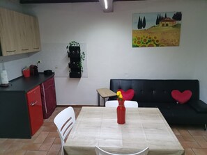 A kitchen with a dining table, chairs, a sofa with heart-shaped cushions, and a painting on the wall.