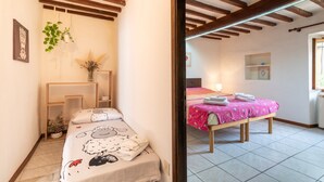 Un dormitorio con cama, mesita de noche, planta colgante y ventana.