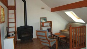 Une pièce chaleureuse avec une cheminée, un lit en mezzanine, un bureau et une bibliothèque.