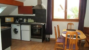 Une cuisine compacte équipée d’un lave-linge, d’un four et d’un coin repas avec des chaises et une table.