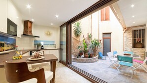 A modern kitchen with a dining area, a large sliding glass door leading to an outdoor patio with chairs and potted plants. - Apartment 'Plaisir Des Pierres' with Private Terrace and Wi-Fi (RIVESALTES)