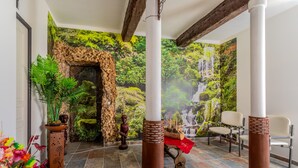 Una habitación con un arco de piedra, un mural de cascada, una estatua de madera y un área de descanso con sillas.