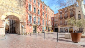 Un patio con suelo de ladrillo, un árbol grande en maceta y edificios históricos con varios pisos y balcones.