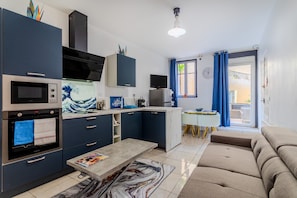 A modern kitchen with dark cabinets, a built-in oven, and a dining area with a white table and blue curtains.