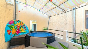 Un área pequeña de piscina al aire libre con un jacuzzi, un colorido paraguas floral y una zona de estar cubierta.
