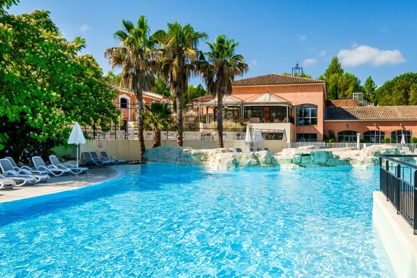 A swimming pool with lounge chairs, palm trees, and a building with a tiled roof.