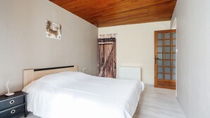 Une chambre avec un plafond en bois, un lit, une table de chevet, un radiateur et une porte en bois.