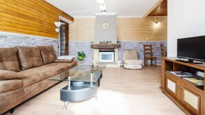 Un salon avec un canapé, une table basse en verre, une cheminée, un téléviseur et un lambris en bois.