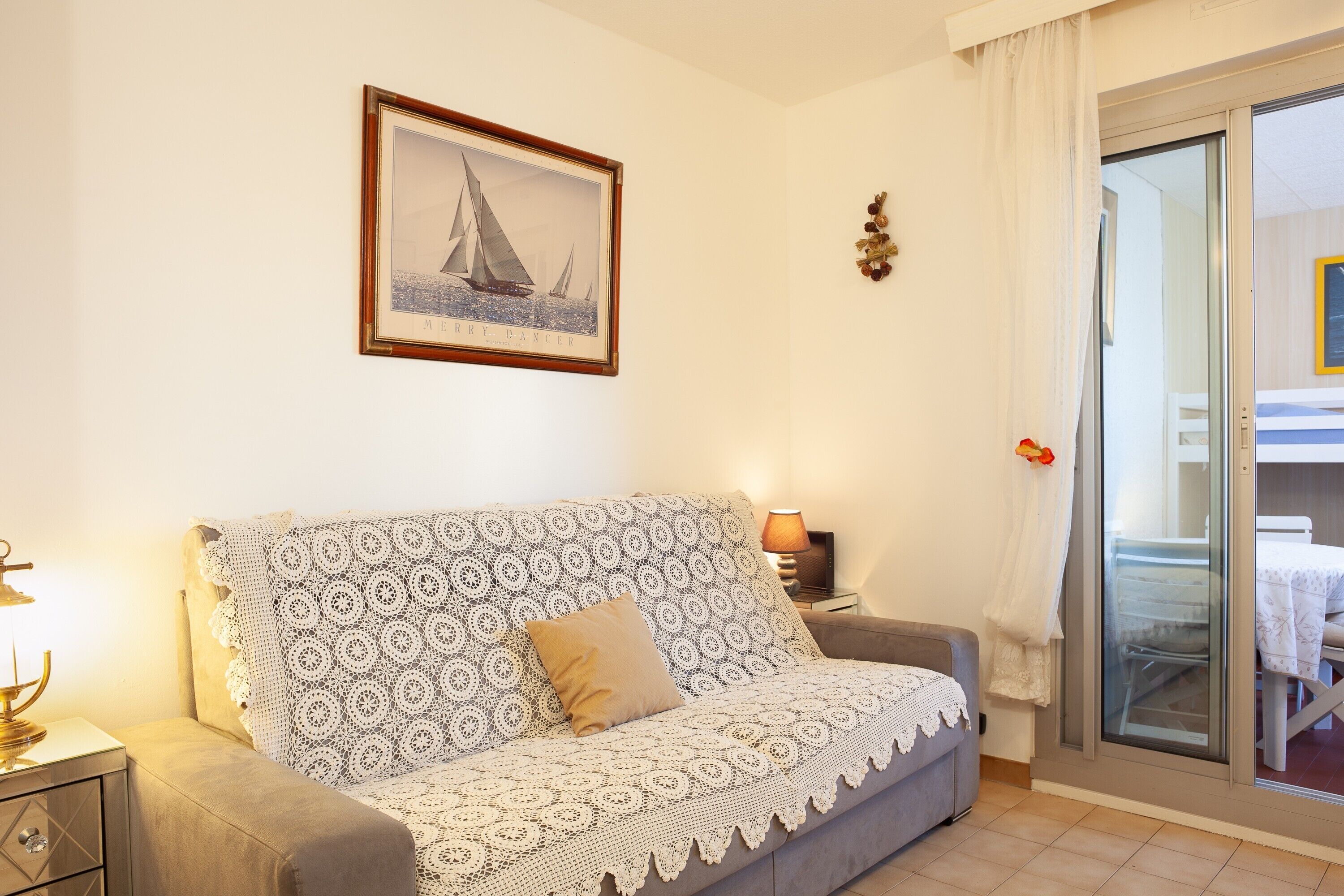 Ein Wohnzimmer mit einer gemusterten Couch, einem gerahmten Bild an der Wand, einer Lampe und einer Glasschiebetür, die auf einen Balkon führt.