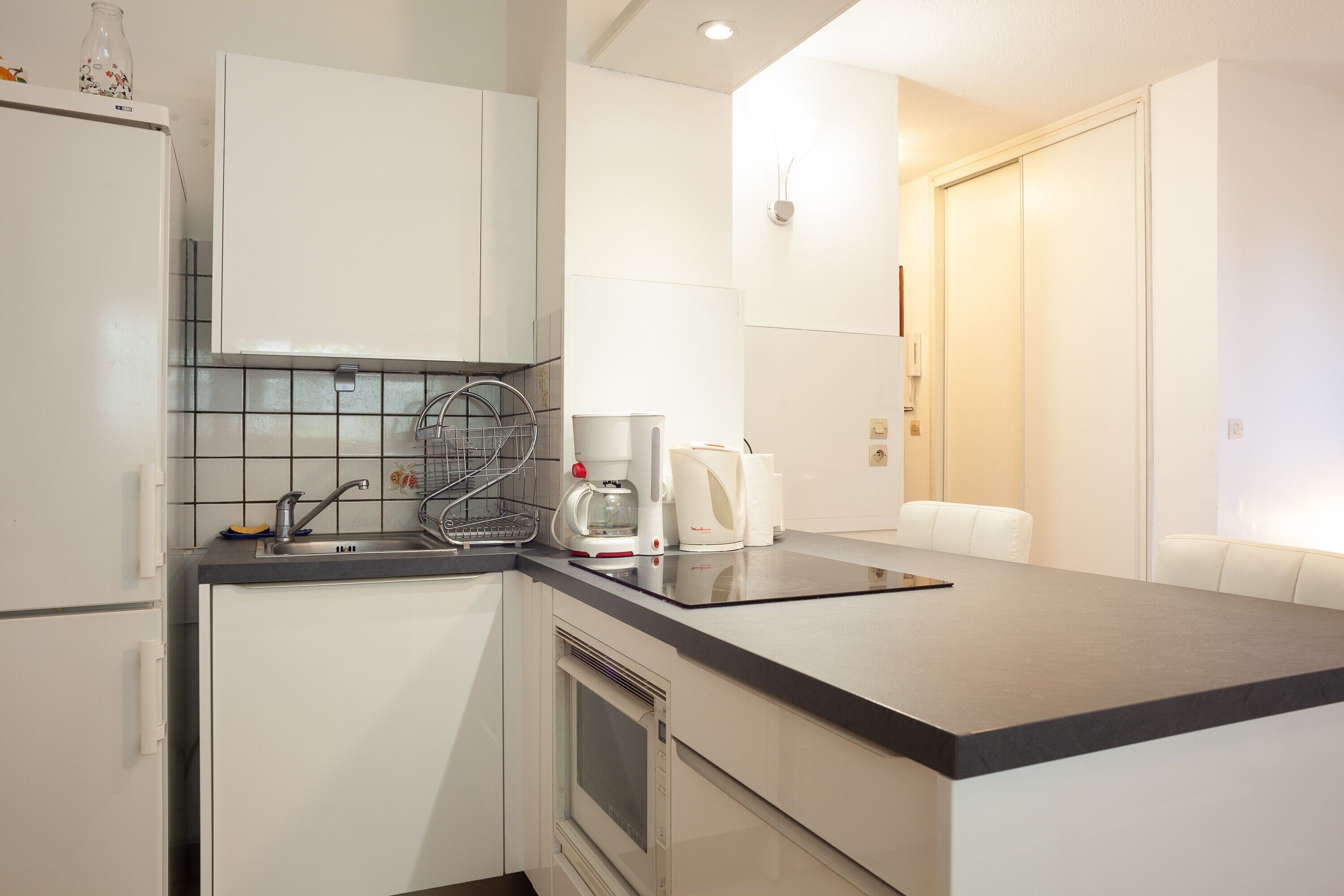 A modern kitchen with white cabinets, a black countertop, a coffee maker, and a microwave.