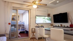 Une chambre d’hôtel moderne dotée d’un balcon, d’un ventilateur de plafond, d’une télévision à écran plat, d’un coin cuisine et d’un espace repas.