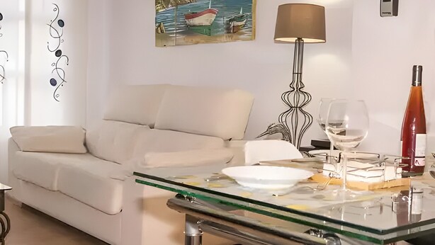 A living room with a glass-top coffee table, a white sofa, a painting of a boat on the wall, a floor lamp, and a wine bottle. - 'Bahía D'Or Plaza' Apartment with Air Conditioning (Chiclana de la Frontera)