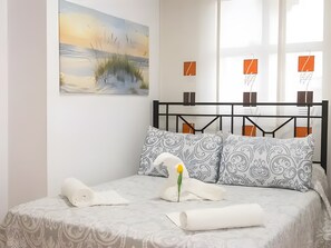 A neatly made bed with patterned pillows, a single flower, and rolled towels.