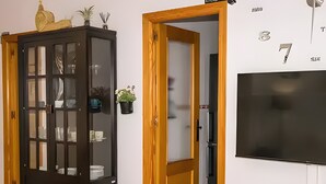 A room with a dark wooden cabinet, a wooden door, a white wall with a TV mounted above it, and a small potted plant. - 'Bahía D'Or Plaza' Apartment with Air Conditioning (Chiclana de la Frontera)