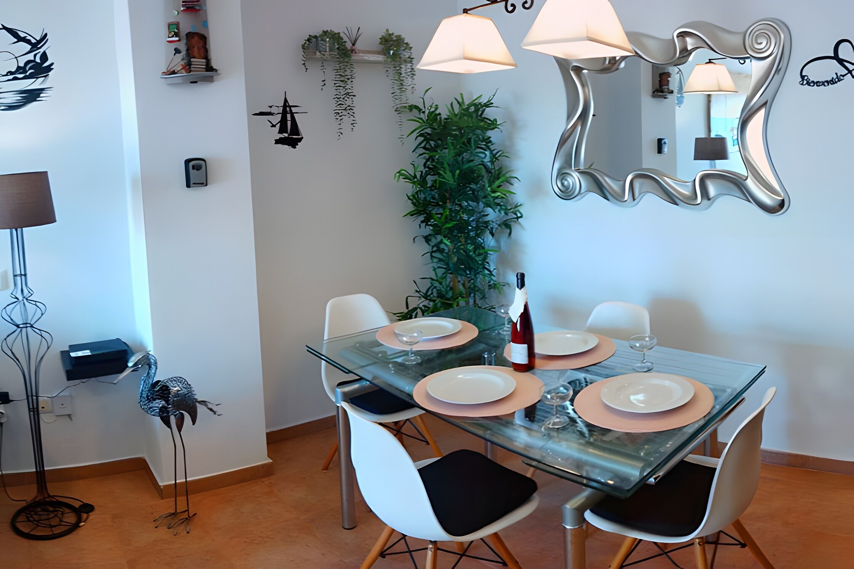 A dining area with a glass table, white chairs, and a mirror on the wall.