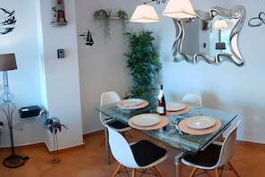 A dining area with a glass table, white chairs, and a mirror on the wall.