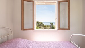 A bedroom with a bed, a window with a view of the sea, and a white wall.