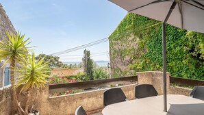 A terrace with a table and chairs, a potted plant, and a view of the sea.