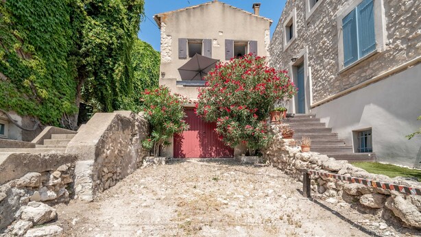 A stone building with a red door, a staircase leading up to it, and a garden with red flowers.