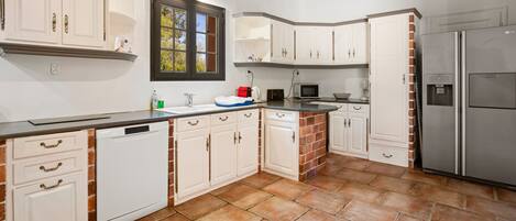 A kitchen with white cabinets, a dishwasher, a microwave, a refrigerator, and a window with a view of greenery.