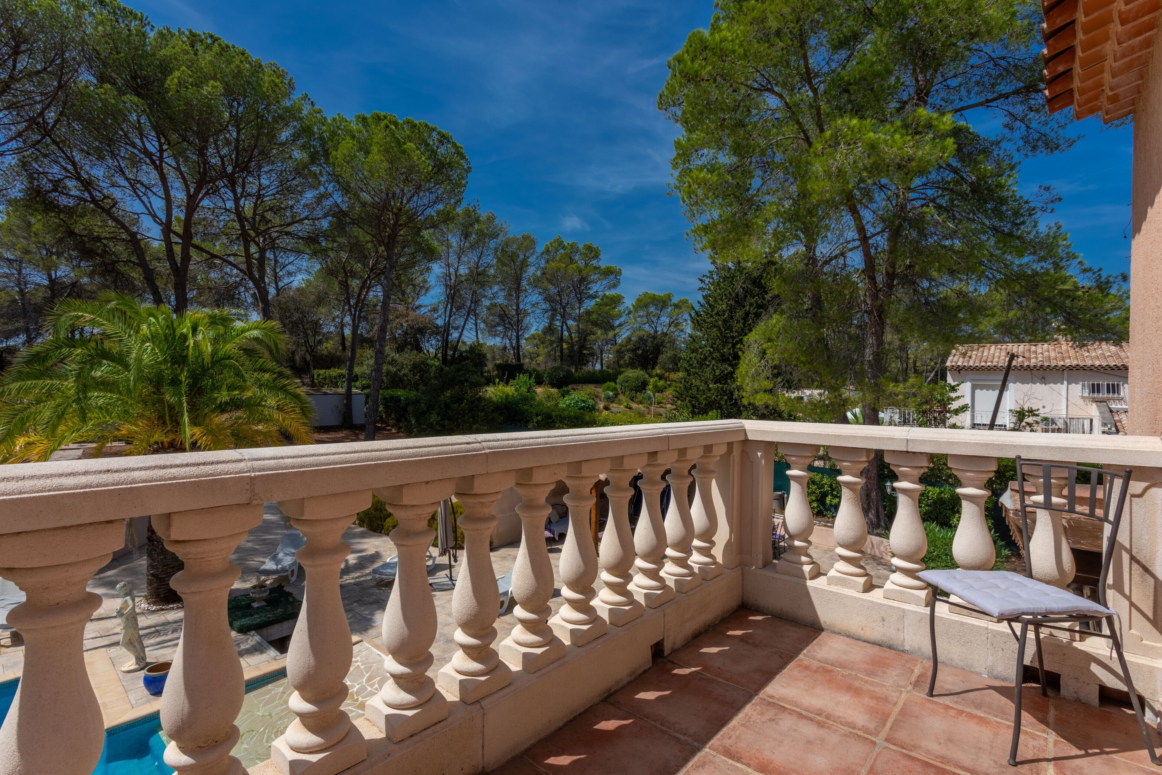 Un balcon doté d’une balustrade en pierre, une piscine et une végétation luxuriante tout autour.