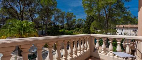 Un balcon doté d’une balustrade en pierre, une piscine et une végétation luxuriante tout autour.