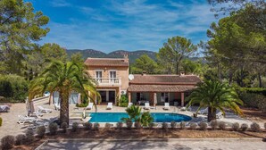 A two-story house with a swimming pool, surrounded by trees and hills.