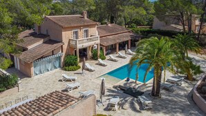 A villa with a swimming pool, sun loungers, and a covered patio area.