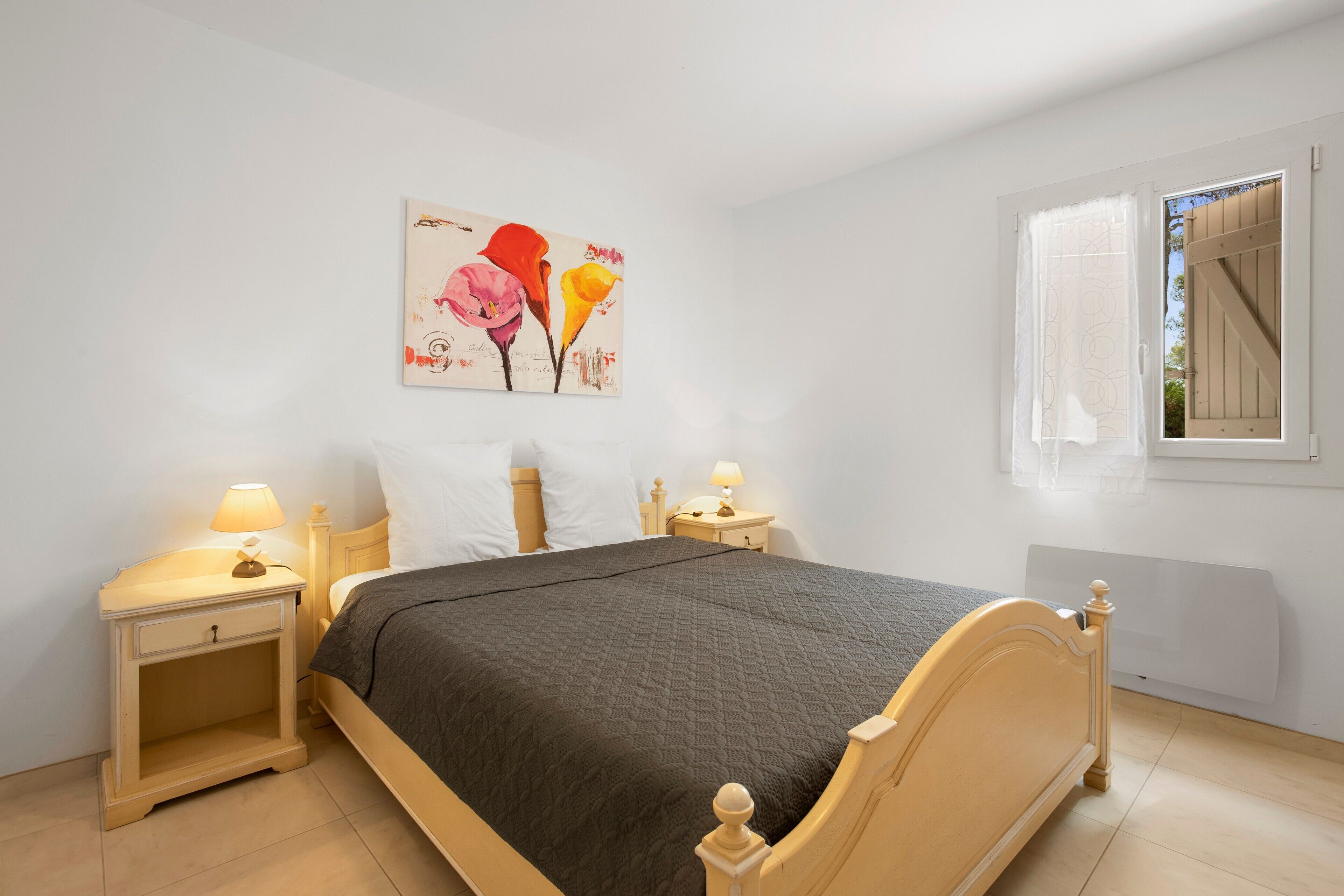 Una camera da letto con un letto, due comodini, una lampada, un quadro appeso al muro e una finestra con tende.