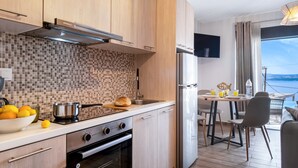 A modern kitchen with wooden cabinets, a tiled backsplash, a built-in oven, and a dining area with a view. - Apartment 'Ionian Sea View Luxury Apartments' with Wi-Fi and Air Conditioning (Lefkada)