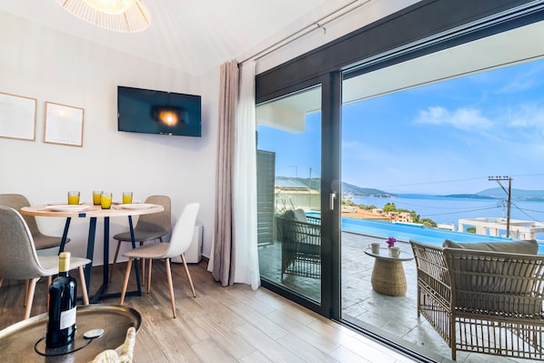 A modern room with a dining area, a TV, and a large glass door leading to a pool.