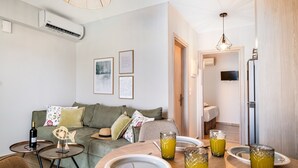 A modern living room with a sofa, a dining table set with plates and glasses, a television, and an air conditioning unit. - Apartment 'Ionian Sea View Luxury Apartments' with Wi-Fi and Air Conditioning (Lefkada)