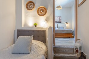 Une chambre à coucher comprenant un lit, une tête de lit, une étagère fixée au mur avec des objets décoratifs, et un couloir menant à une autre pièce.
