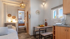 Ein Schlafzimmer mit Bett, Nachttisch und einer Ablage. In der Ecke steht ein kleiner Tisch mit Obstschale und Blumenvase. Ein Fenster mit Vorhängen ist zu sehen, und eine Uhr ist an der Wand befestigt.