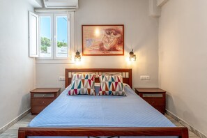 Une chambre à coucher avec un lit, deux tables de chevet, une fenêtre et un tableau accroché au mur.