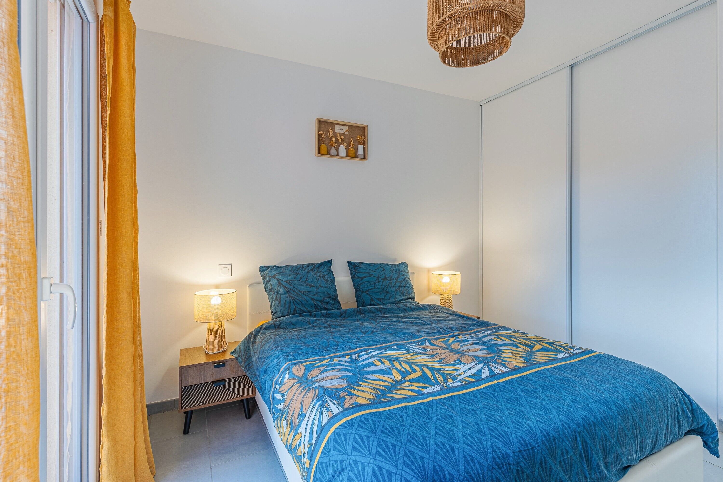 Ein Schlafzimmer mit einem Bett, zwei Nachttischlampen, einem Nachttisch, einer Wandablage mit Dekoration und einer Deckenleuchte.