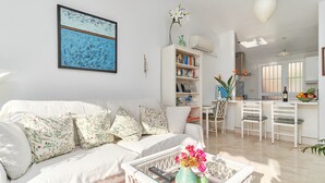 Una sala de estar con un sofá blanco, una mesa de centro con un jarrón de flores y una estantería.