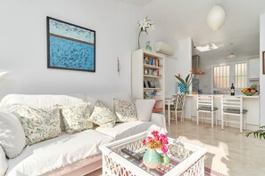 Un salon avec un canapé blanc, une table basse ornée d’un vase de fleurs et une bibliothèque.