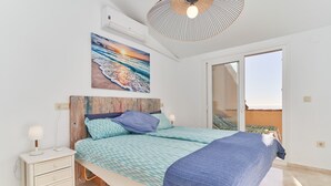 Un dormitorio con cama, mesita de noche, una obra de arte en la pared y vistas a través de una puerta corrediza.
