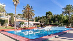 Una piscina con borde rojo, rodeada de palmeras y un edificio con balcones.