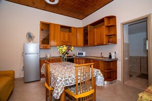 A compact kitchen with wooden cabinets, a refrigerator, a microwave, and a dining table with chairs.