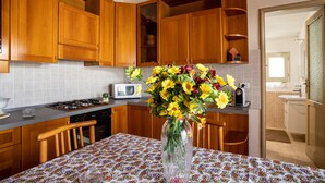 Une cuisine avec des meubles de rangement en bois, un four à micro-ondes, un vase de fleurs et une nappe à motifs.