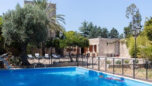 A swimming pool with a fence, lounge chairs, and a stone building in the background.