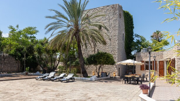 A courtyard with stone walls, palm trees, lounge chairs, and outdoor seating.